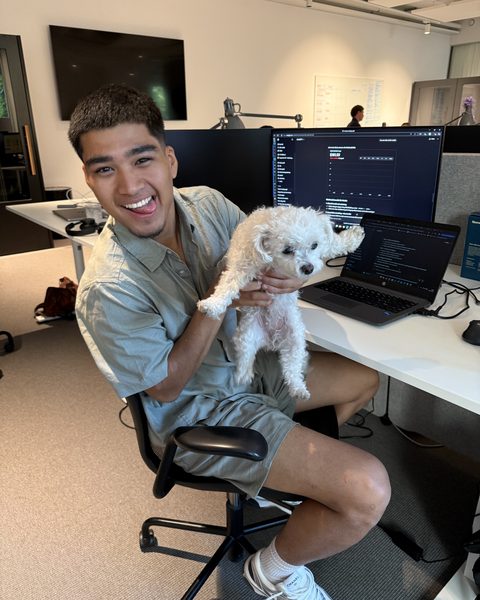 A developer turning from his screen, holding a small white dog.