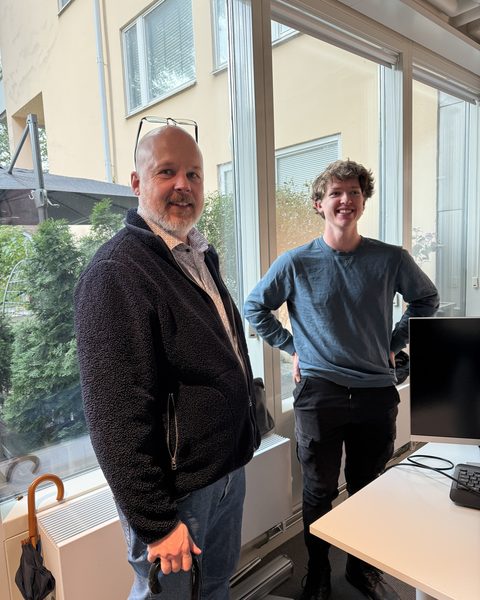 Peter and Viggo standing by the office window beside a desk.